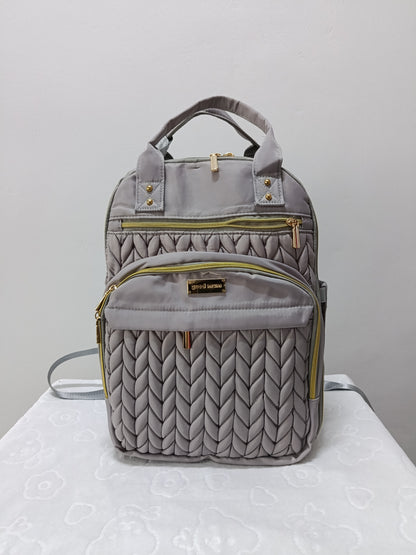 A gray quilted backpack with gold-tone zippers and hardware, featuring top handles and a front pocket, displayed on a white surface against a light gray background.