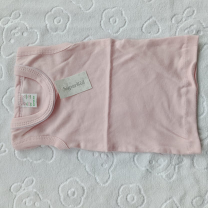 A light pink baby tank top laid flat on a white textured blanket with a floral pattern. The shirt has a visible 'Superkid' brand label and a size tag.