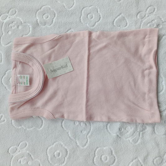 A light pink baby tank top laid flat on a white textured blanket with a floral pattern. The shirt has a visible 'Superkid' brand label and a size tag.